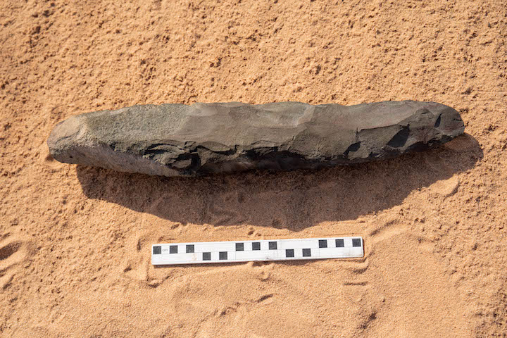 Large Acheulean hand axe from AlUla region on desert sand with scale bar